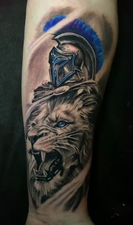 Custom realistic tattoo blending a roaring lion and Spartan helmet with blue highlights, crafted by Elvis Tattoo Shop.